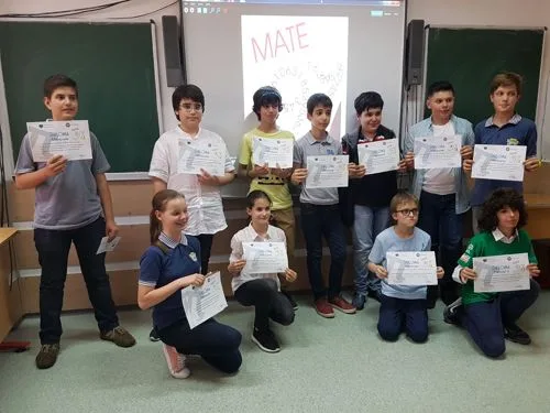 Elevi cu diplome într-o sală de clasă, în fața unui ecran cu inscripția MATE